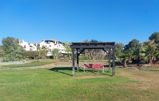 Un jardín con un banco de madera y un árbol al fondo.