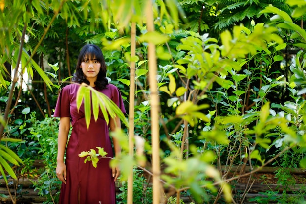 Jardín forestal en el concepto de estilo relajante de vestido morado de mujer india. El pelo corto negro femenino asiático de los años 20 siente una sonrisa feliz en la granja de bambú verde. La mujer permanece tranquila en el entorno natural de verano