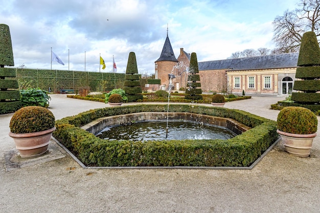 Foto jardín francés con una fuente en la torre del castillo de alden biesen, paredes de ladrillo y techo a dos aguas, árboles cortados en forma cónica del siglo xvi, día nublado en bilzen, limburgo, bélgica