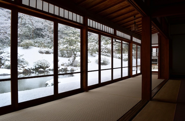 Jardín de invierno japonés visto desde el interior de una habitación tradicional con ventanas panorámicas