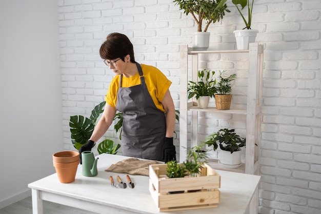 Jardineira de meia idade transplantando planta em vasos de cerâmica no conceito de mesa de madeira branca de