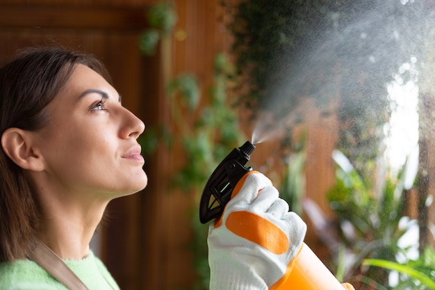 Jardineira em casa com avental e luvas com plantas em crescimento na varanda da casa regando com spray