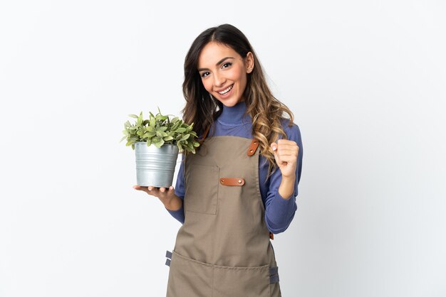 Jardineira segurando uma planta em fundo branco comemorando vitória na posição de vencedora