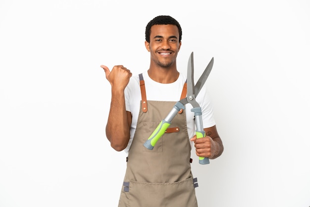 Jardineiro afro-americano segurando uma tesoura de poda sobre um fundo branco isolado apontando para o lado para apresentar um produto