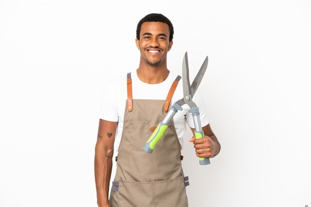 Jardineiro afro-americano segurando uma tesoura de poda sobre um fundo branco isolado, posando com os braços na cintura e sorrindo