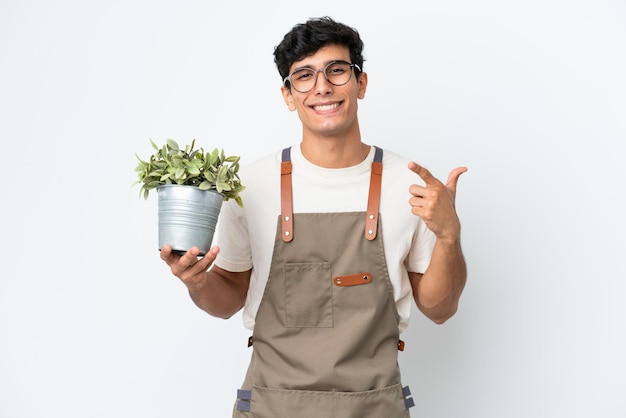 Jardineiro argentino segurando uma planta isolada no fundo branco e fazendo um gesto de polegar para cima