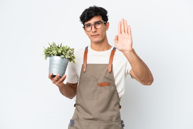 Jardineiro argentino segurando uma planta isolada no fundo branco fazendo gesto de pare