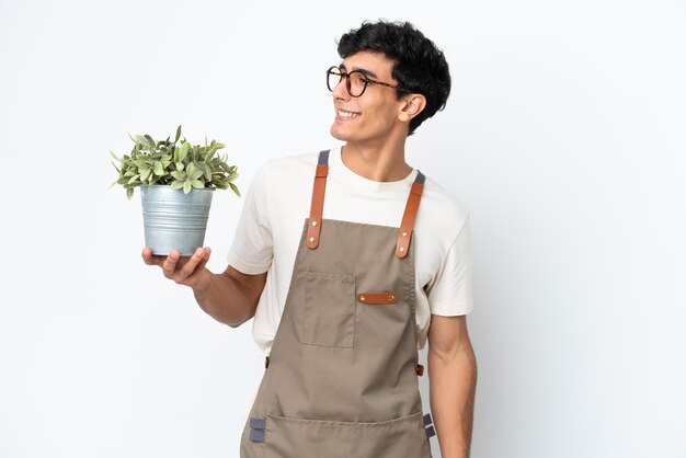 Jardineiro argentino segurando uma planta isolada no fundo branco, olhando para o lado e sorrindo