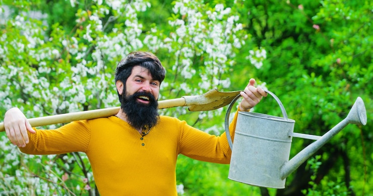 Foto jardineiro barbudo com regador e pá preparando-se para plantar agricultor trabalhando no jardim primavera