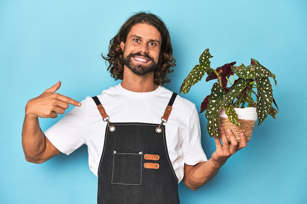 Foto jardineiro de cabelos longos com barba segurando uma planta apontando com a mão para um espaço de cópia de camisa