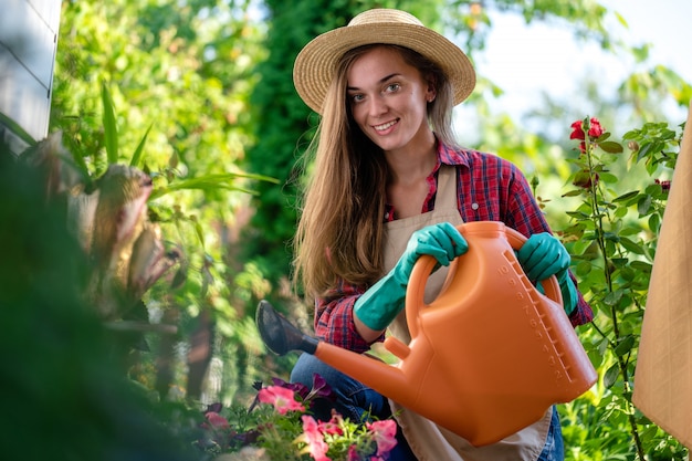 Jardineiro de chapéu e avental usando regador para regar flores no jardim de casa. jardinagem e floricultura