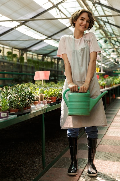 Jardineiro de mulher bonita e fofa em pé sobre as plantas na estufa de flores aquáticas