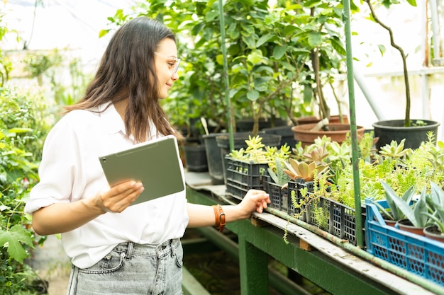 Jardineiro de mulheres de negócios atraentes de óculos usando tecnologia moderna de tablet em negócios de jardinagem