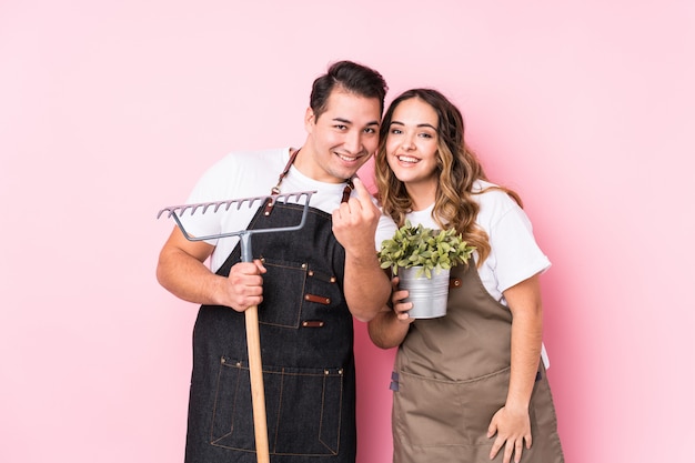 Jardineiro jovem casal apontando com o dedo para você, como se convidando se aproximar.