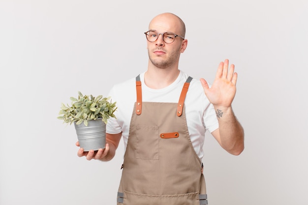 Jardineiro parecendo sério, severo, descontente e irritado mostrando a palma da mão aberta fazendo gesto de pare