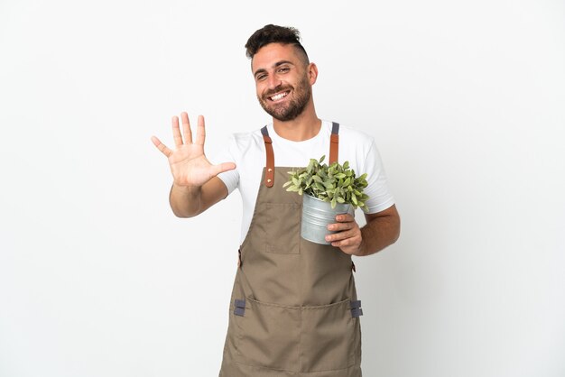 Jardineiro segurando uma planta sobre um fundo branco isolado, contando cinco com os dedos