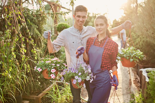 Foto jardineiros de rapaz e moça felizes segurar vasos com petúnia no maravilhoso jardim em um dia ensolarado. .