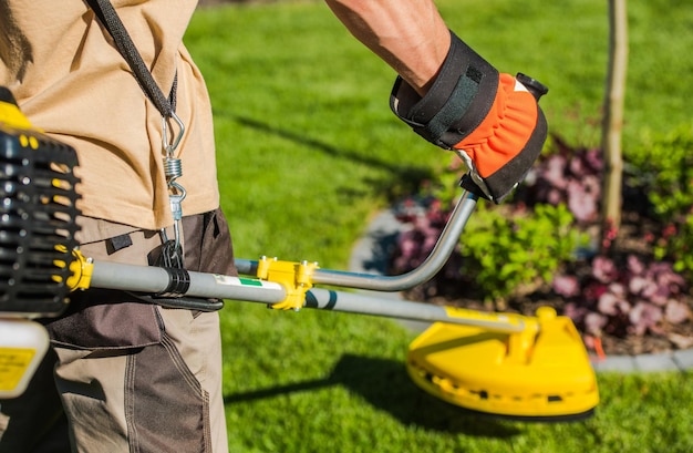 Jardiner caucásico con cortador de cepillos de gasolina y cortador de cuerdas en su hombro recortando el jardín