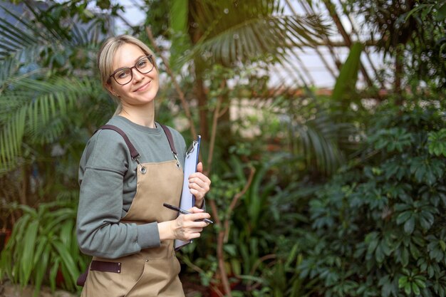 Una jardinera en un delantal trabaja en el centro de jardinería, la floristería trabaja en un invernadero Espacio para texto