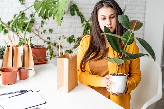 Jardinería doméstica. Pequeños negocios. Jardinero joven cuidando las plantas poniendo una maceta en la bolsa de artesanía lista para venderla