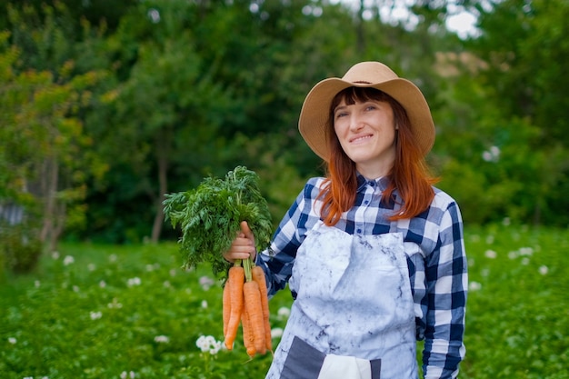 Jardinería - Hermosa mujer joven con zanahorias orgánicas en un huerto. iluminar desde el fondo