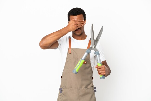 Jardinero afroamericano hombre sosteniendo tijeras de podar sobre fondo blanco aislado cubriendo los ojos con las manos. No quiero ver algo