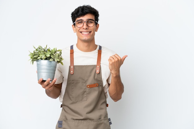 Jardinero argentino sosteniendo una planta aislada sobre fondo blanco apuntando hacia el lado para presentar un producto