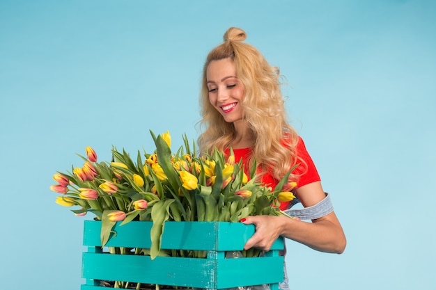 Jardinero de hermosa mujer rubia con caja con tulipanes en superficie azul