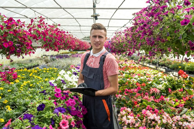 Jardinero hombre vistiendo uniforme trabajando con flores decorativas en una maceta en un invernadero de plantas industriales