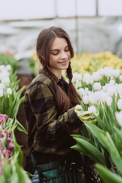 Jardinero joven cuidando flores de tulipanes cultivados en invernadero.