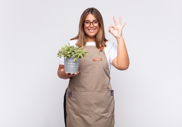 Jardinero joven que se siente feliz, relajado y satisfecho, mostrando aprobación con gesto bien, sonriendo