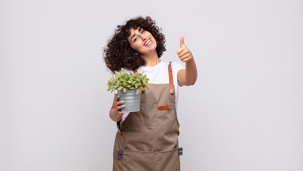 Jardinero joven que se siente orgulloso, despreocupado, seguro y feliz, sonriendo positivamente con los pulgares hacia arriba