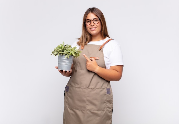 Jardinero joven sonriendo alegremente, sintiéndose feliz y apuntando hacia un lado y hacia arriba