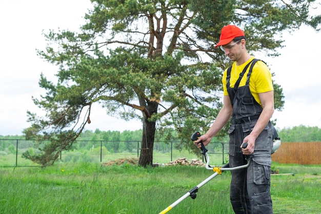 Un jardinero masculino corta la hierba verde del césped en el patio trasero con un cortacésped de gasolina Trimmer para el cuidado de una parcela de jardín