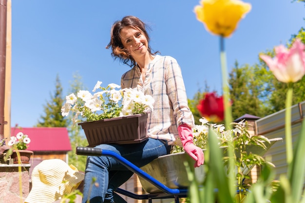 Jardinero de mujer con flores. Planta plántulas en el jardín de su casa. El granjero sostiene los brotes.