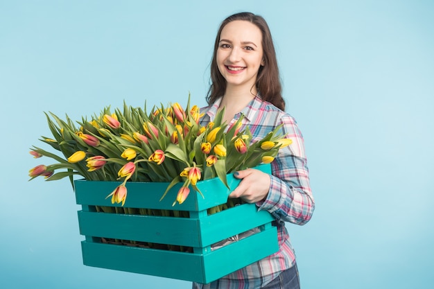 Jardinero mujer hermosa con caja con tulipanes sobre fondo azul.