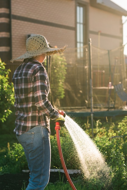 Jardinero de mujer en ropa de trabajo regando las camas en su huerto en un día soleado de verano. Concepto de trabajo en el jardín y su granja.