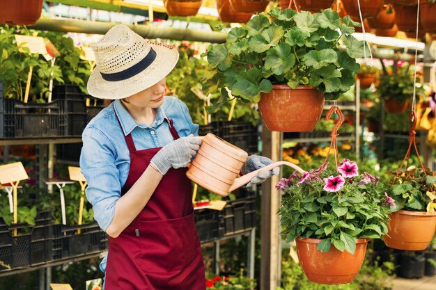 Jardinero de mujer con sombrero y guantes trabaja con flores en el invernadero