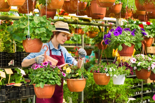 Jardinero de mujer con sombrero y guantes trabaja con flores en el invernadero