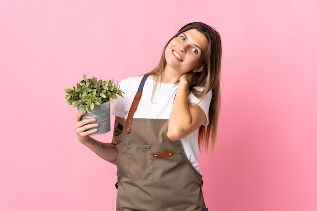 Jardinero mujer sosteniendo una planta aislada en rosa riendo