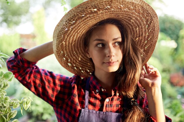 Jardinero de niña encantadora con un sombrero de paja está de pie en el maravilloso jardín en un día soleado. .