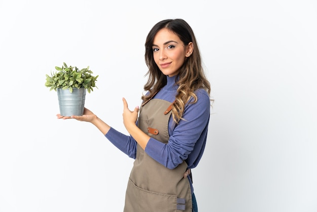 Jardinero niña sosteniendo una planta aislada en un espacio en blanco apuntando hacia atrás