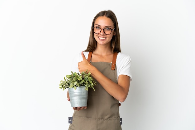 Jardinero niña sosteniendo una planta sobre fondo blanco aislado dando un gesto de pulgar hacia arriba