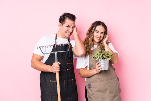 Jardinero de pareja joven aislado cubriendo las orejas con las manos