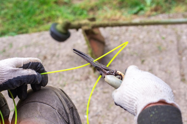 Un jardinero con una podadora corta un trozo de hilo de pescar para una cortadora de césped a gas Cuidado del césped de corte de césped de primavera