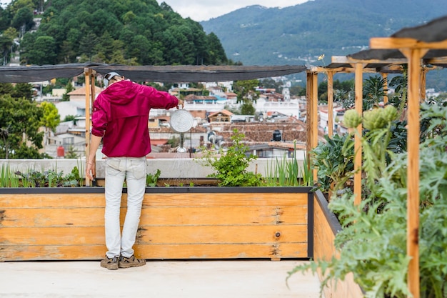 Jardinero regando plantas en una terraza con huerto urbano.