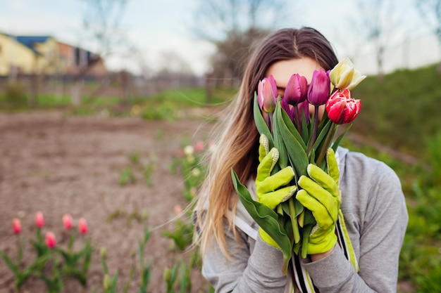 Jardinero sosteniendo un ramo de tulipanes frescos en el jardín de primavera Mujer joven escondiendo la cara detrás de las flores