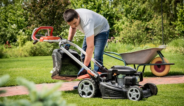 Foto jardinero vaciando el césped del cortacésped en una carretilla después de cortar el césped. diseño de exteriores. jardinería