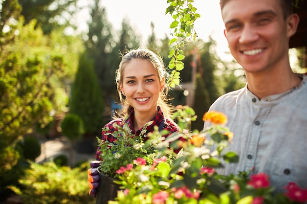 Los jardineros niño y niña felices sostienen macetas con plantas en hermosos jardines en un día cálido y soleado.