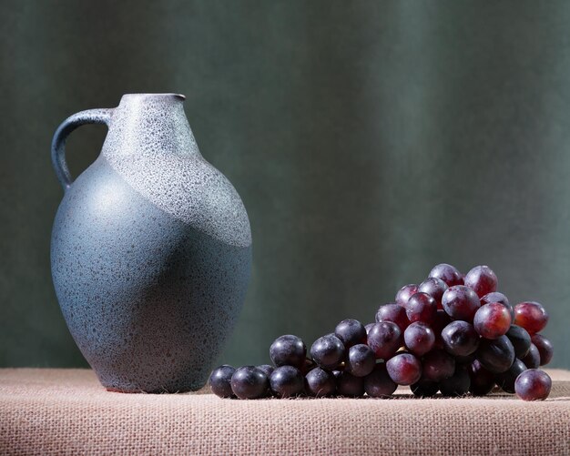 Una jarra azul y uvas están sobre una mesa.